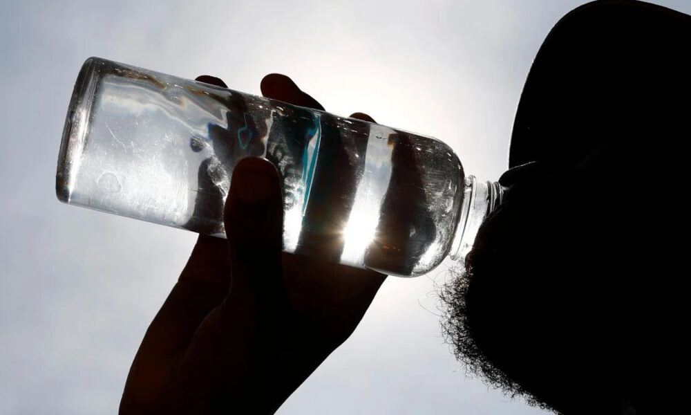 Silhouette of a person drinking from a plastic water bottle against a bright sky.