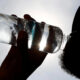Silhouette of a person drinking from a plastic water bottle against a bright sky.