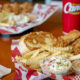 Fried chicken, fries, onion rings, coleslaw, and two dipping sauces on a red-tray meal at a fast-food joint.