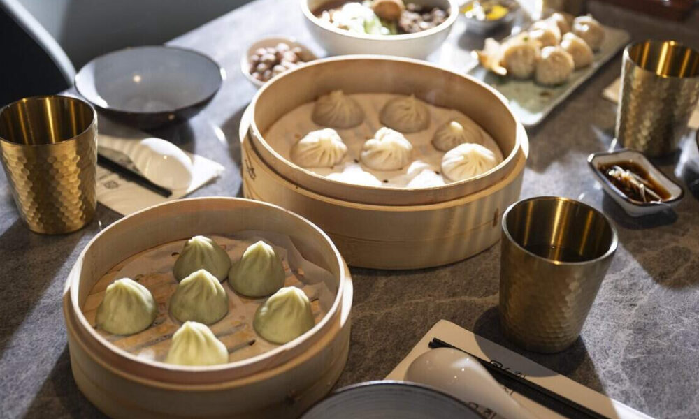 Dim sum feast: bamboo steamers filled with green and white dumplings on a dining table with cups nearby.