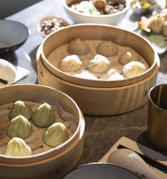 Dim sum feast: bamboo steamers filled with green and white dumplings on a dining table with cups nearby.