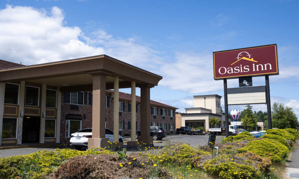 Exterior view of Oasis Inn hotel with a covered driveway and parked cars on a sunny day.