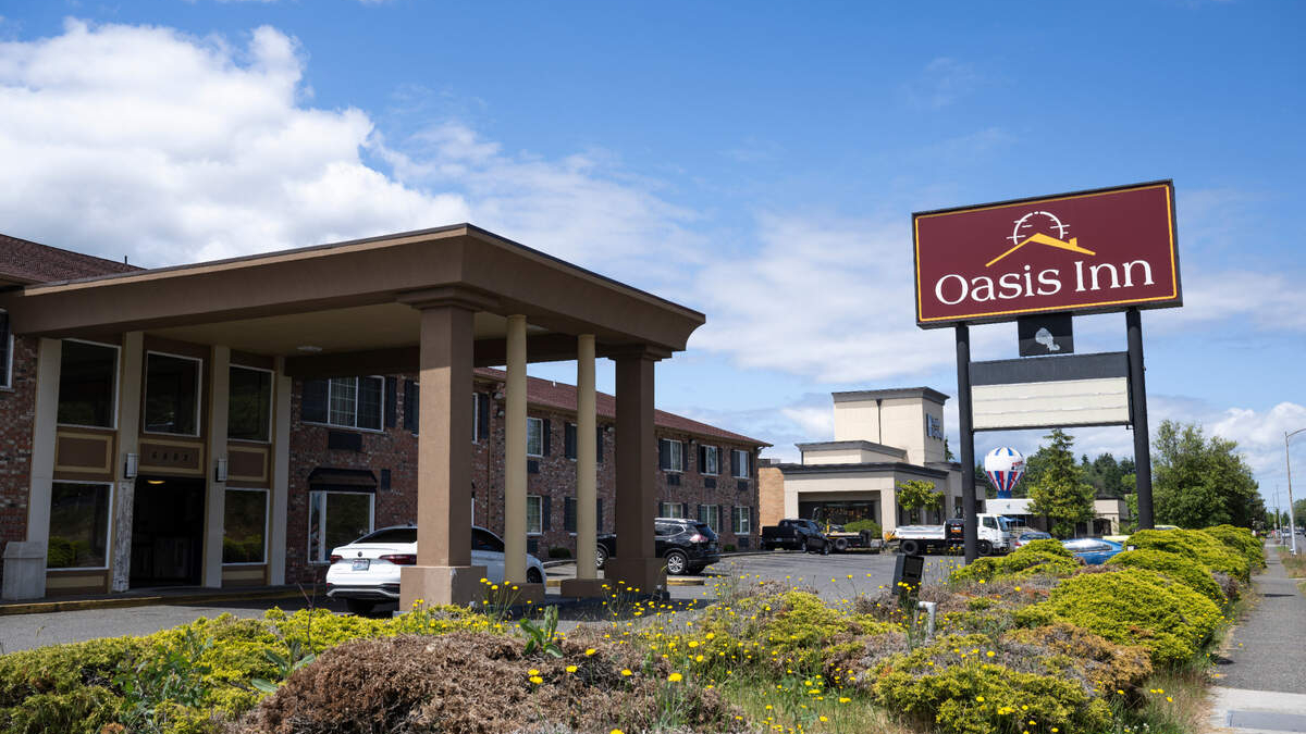 Exterior view of Oasis Inn hotel with a covered driveway and parked cars on a sunny day.