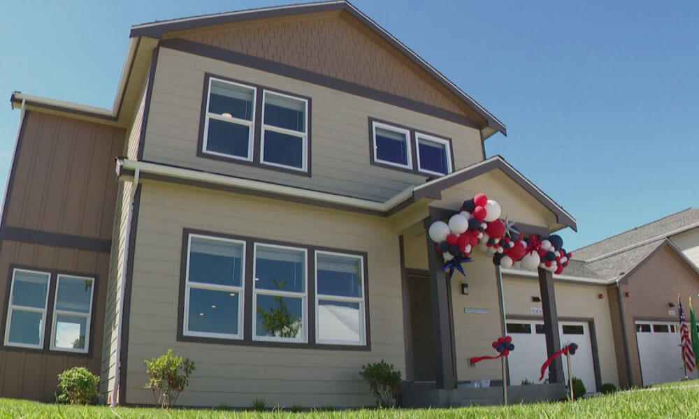 Two-story beige house with red, white, and blue balloons decorating the front porch for a celebration behind a clear blue sky.