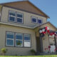 Two-story beige house with red, white, and blue balloons decorating the front porch for a celebration behind a clear blue sky.