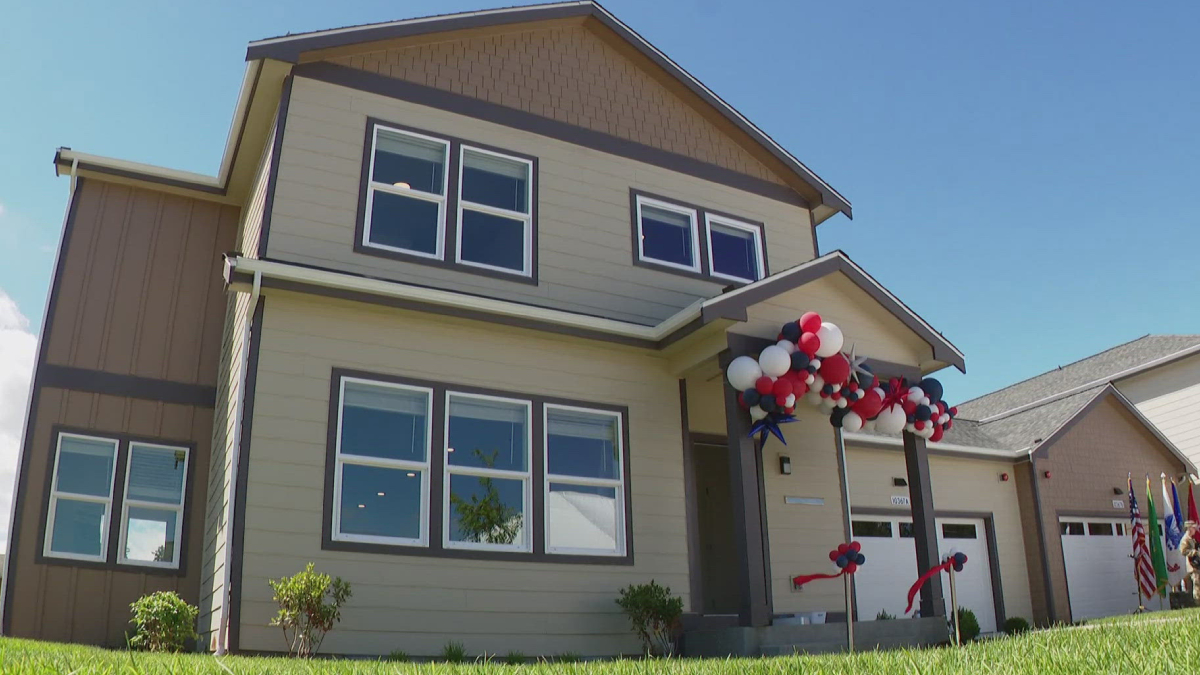 Two-story beige house with red, white, and blue balloons decorating the front porch for a celebration behind a clear blue sky.