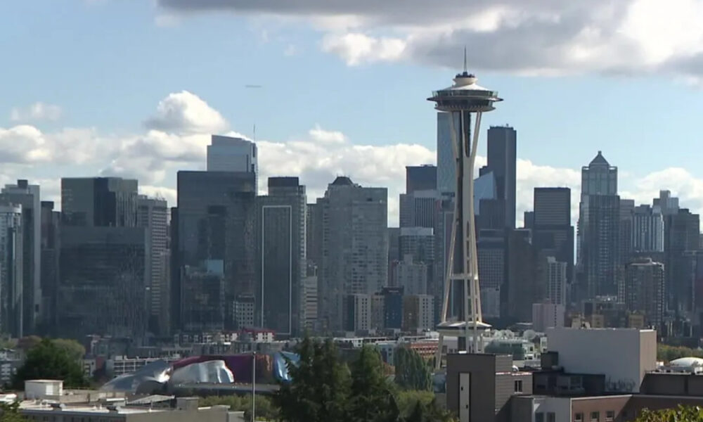 Seattle skyline with the Space Needle towering over downtown against a blue sky with scattered clouds.