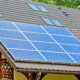 Blue solar panels installed on a sloped residential roof beside a brick chimney and wooden balcony railing