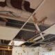 Ceiling with exposed pipes and missing tiles, plus hanging bee and butterfly decorations in a room under renovation.