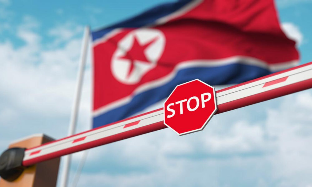 Barrier arm with a red STOP sign; blurred North Korea flag in the background.