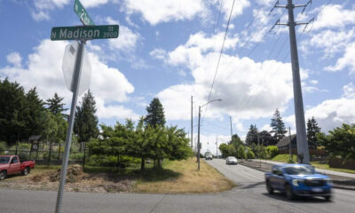 Intersection at N Madison St and N 21st St with green street signs against a blue sky, suburban road and trees nearby.