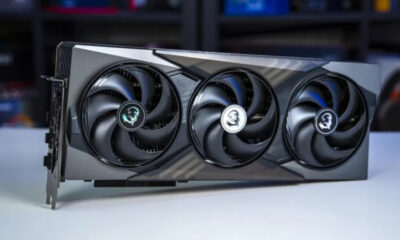 MSI triple‑fan graphics card with a black and gray shroud resting on a white table, showing three cooling fans with MSI dragon logos at the center caps