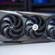 MSI triple‑fan graphics card with a black and gray shroud resting on a white table, showing three cooling fans with MSI dragon logos at the center caps