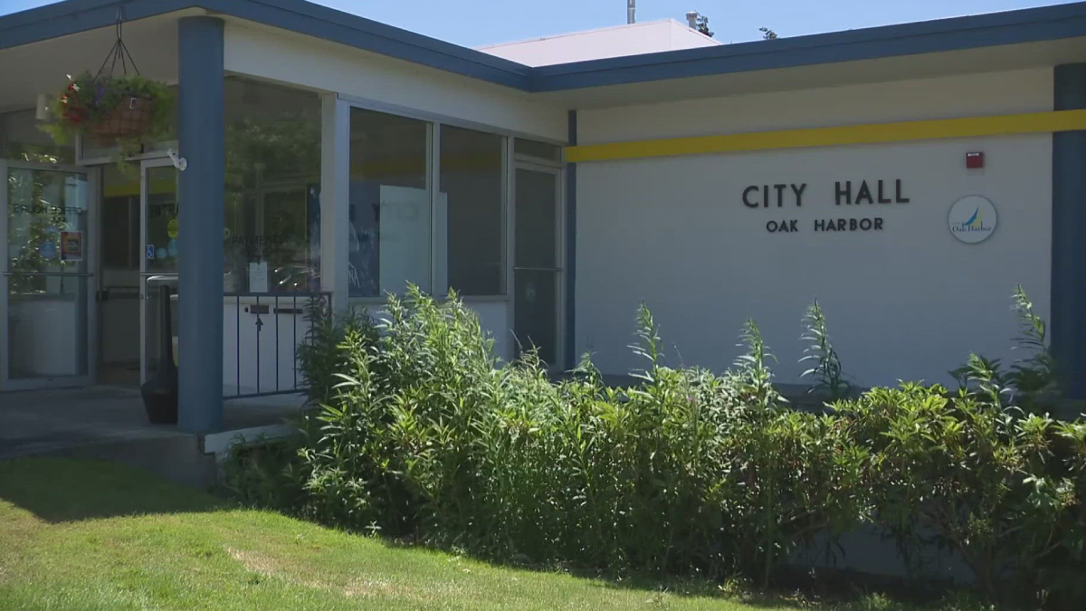 Exterior of City Hall Oak Harbor with glass doors and blue columns, surrounded by greenery in front.