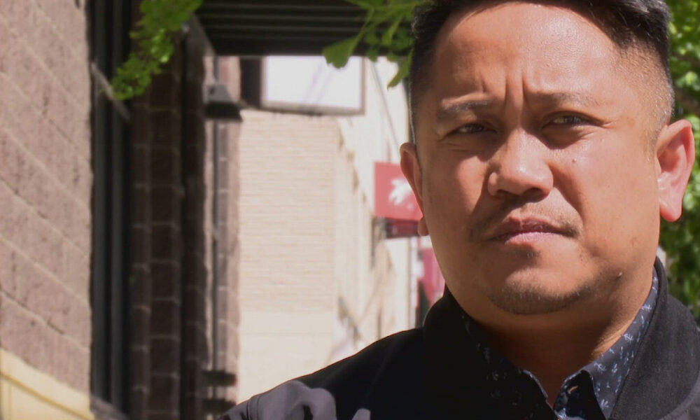 Close-up portrait of a man with short black hair outdoors on a sunny day, looking toward the camera.