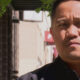 Close-up portrait of a man with short black hair outdoors on a sunny day, looking toward the camera.