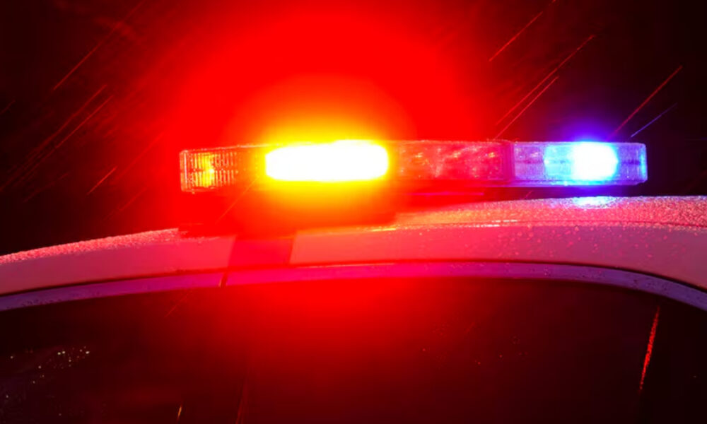 Close-up of a police car with red and blue emergency lights flashing at night under wet weather conditions.