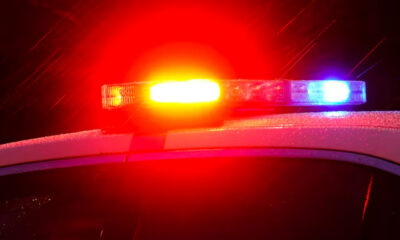 Close-up of a police car with red and blue emergency lights flashing at night under wet weather conditions.