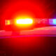 Close-up of a police car with red and blue emergency lights flashing at night under wet weather conditions.