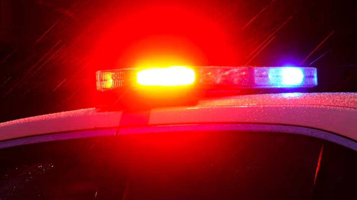 Close-up of a police car with red and blue emergency lights flashing at night under wet weather conditions.