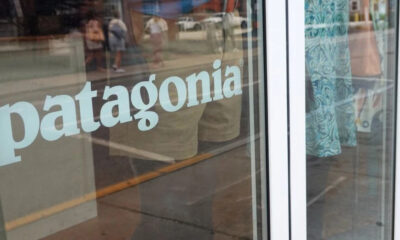 Patagonia storefront window with the brand name visible on glass and reflections of passersby outside.