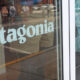 Patagonia storefront window with the brand name visible on glass and reflections of passersby outside.