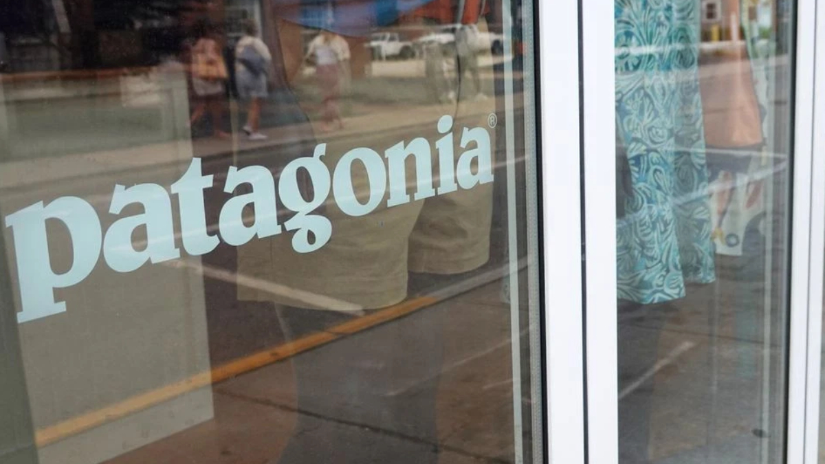 Patagonia storefront window with the brand name visible on glass and reflections of passersby outside.
