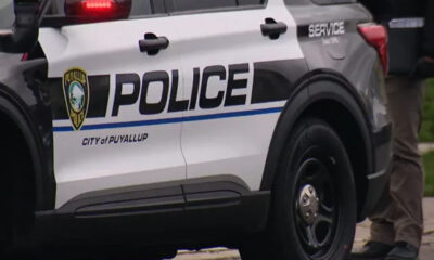 Puyallup Police SUV parked on a street with bold POLICE lettering and city emblem on the door, officer visible nearby legs only.
