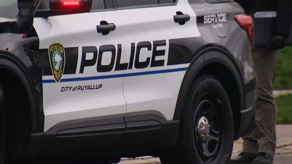 Puyallup Police SUV parked on a street with bold POLICE lettering and city emblem on the door, officer visible nearby legs only.