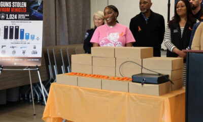 Group of people stand behind a table piled with brown cardboard boxes at a gun-violence awareness event, smiling.