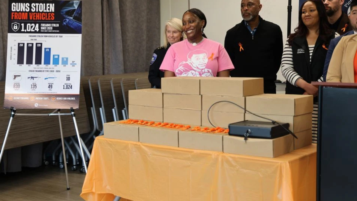 Group of people stand behind a table piled with brown cardboard boxes at a gun-violence awareness event, smiling.