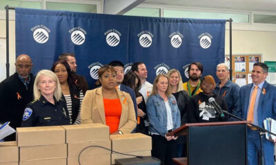 Group of diverse officials and community members at a press conference in front of a Pierce County backdrop, with stacked boxes on the table and a podium with microphones.