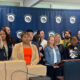 Group of diverse officials and community members at a press conference in front of a Pierce County backdrop, with stacked boxes on the table and a podium with microphones.