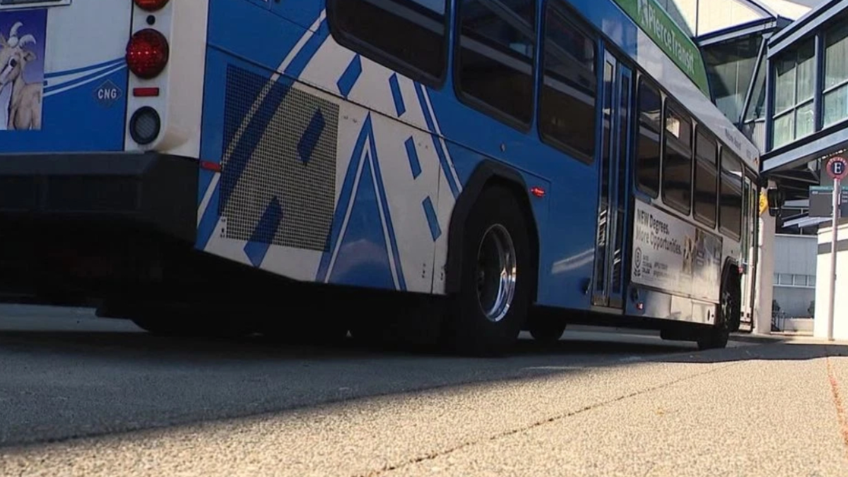 Low-angle side view of a blue city bus parked at a station, with wheels and rear lights visible and white geometric graphics on the side.