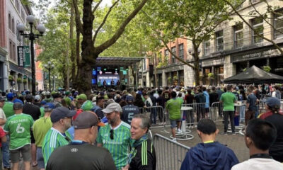 Crowd gathered along a city street watching a live concert on a stage with performers.