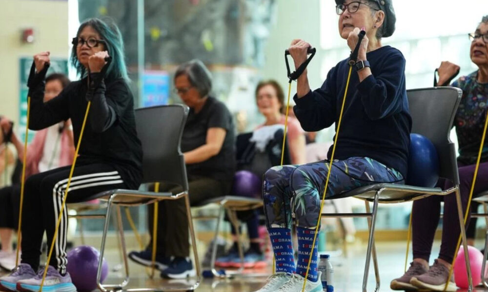 Group of seniors seated in chairs using yellow resistance bands for a seated exercise class in a gym or community center.