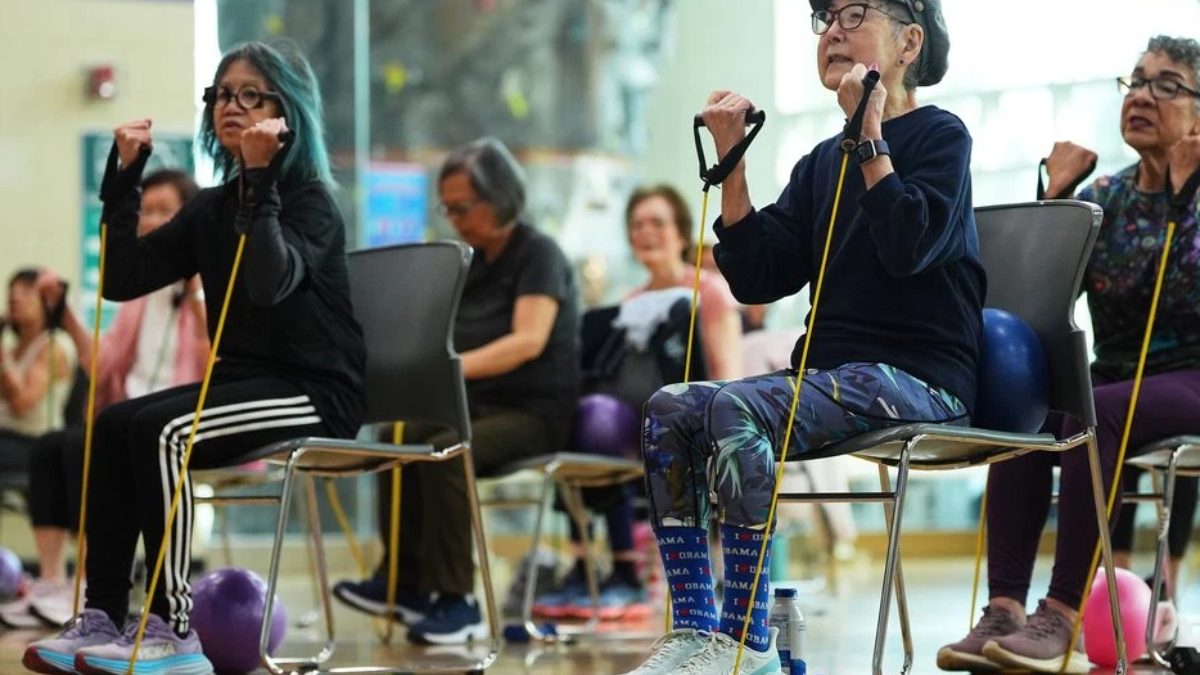 Group of seniors seated in chairs using yellow resistance bands for a seated exercise class in a gym or community center.