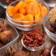 Assorted dried fruits in glass bowls (apricots, raisins, dates) arranged on a rustic wooden surface.