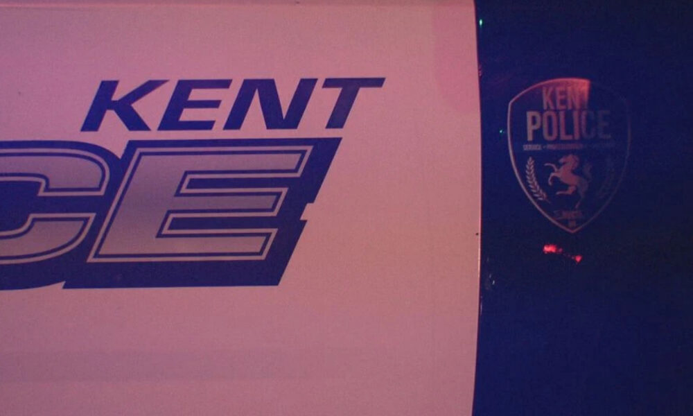Sign with 'KENT' and large stylized letters beside a Kent Police shield logo on a dark background.