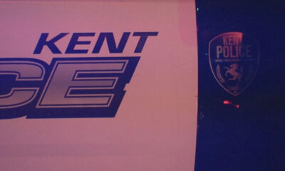Sign with 'KENT' and large stylized letters beside a Kent Police shield logo on a dark background.