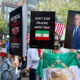 Protesters hold bold signs at a street rally, including 'No deal with murderers' and 'Don’t stop speaking about Iran' with an Iranian flag nearby.