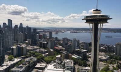 Seattle skyline featuring the Space Needle beside a river and high-rise buildings under a cloudy blue sky.
