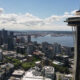 Seattle skyline featuring the Space Needle beside a river and high-rise buildings under a cloudy blue sky.