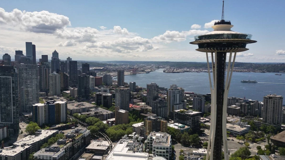 Seattle skyline featuring the Space Needle beside a river and high-rise buildings under a cloudy blue sky.