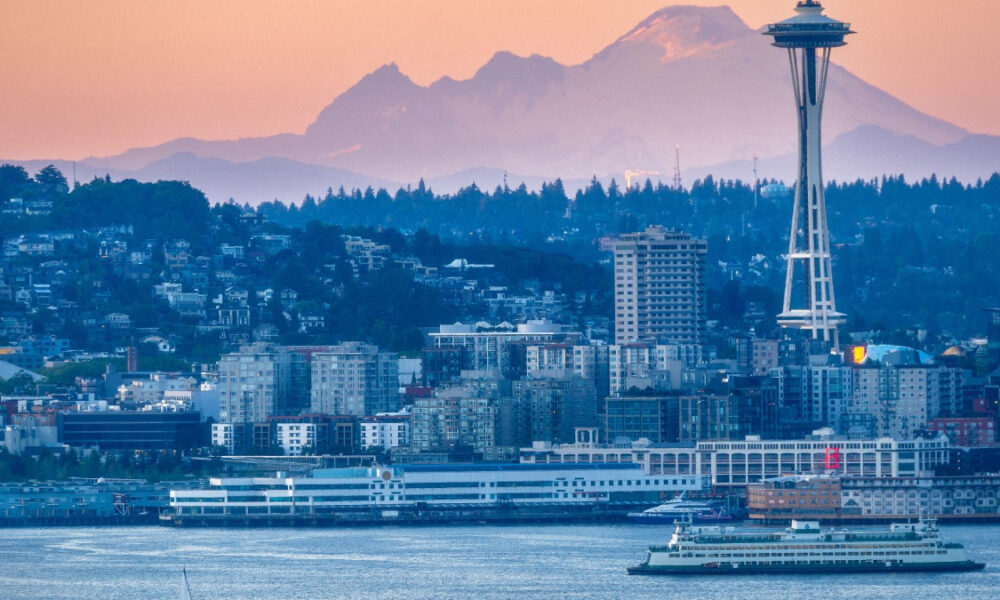 Seattle skyline at sunset with the Space Needle, water in the foreground, and a ferry on the bay