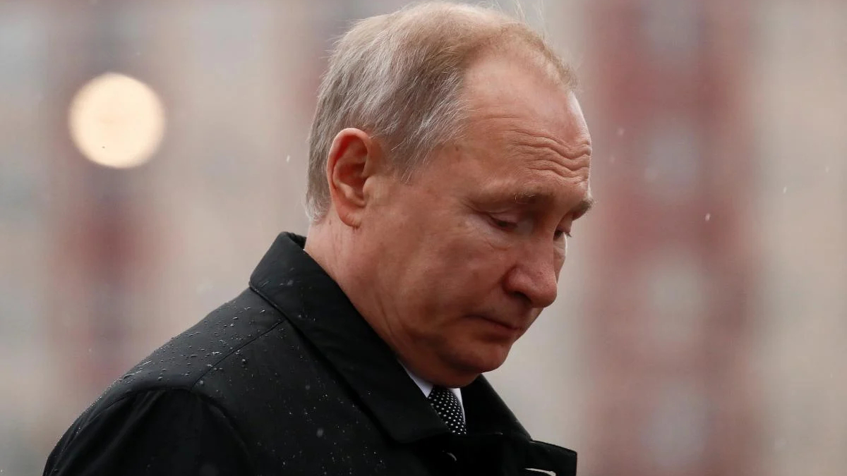Man in a dark coat looking downward in light rain.