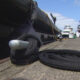 Close-up of a braided mooring rope looped around a silver bollard on a wooden marina dock, with boats in the background.