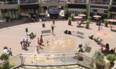 Public square with a circular fountain and people walking around on a sunny day in a mall courtyard.