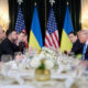 World leaders seated at a long formal table, with Ukrainian and American flags in the background, during a diplomatic meeting.