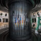 Technician in a cleanroom suit repairin​g equipment inside a large cylindrical vacuum chamber inside a laboratory.